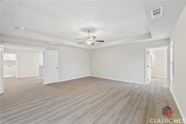 spare room with a tray ceiling, ceiling fan, and light hardwood / wood-style floors