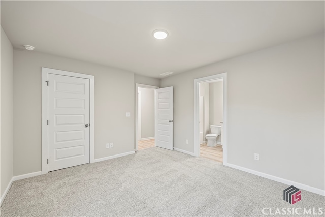 unfurnished bedroom featuring light carpet, ensuite bath, and a closet