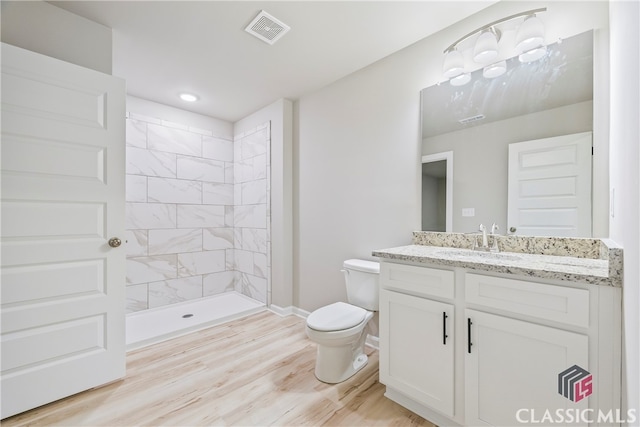 bathroom with hardwood / wood-style floors, vanity, toilet, and tiled shower