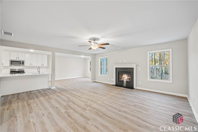 unfurnished living room with ceiling fan, light wood-type flooring, and sink