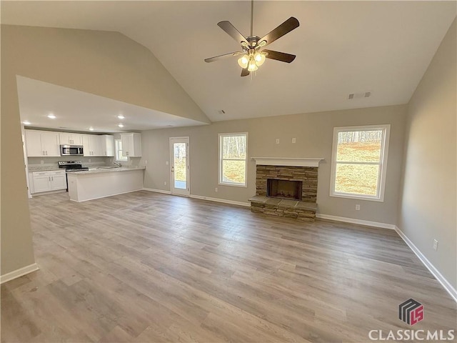 unfurnished living room with ceiling fan, a fireplace, a healthy amount of sunlight, and light hardwood / wood-style flooring