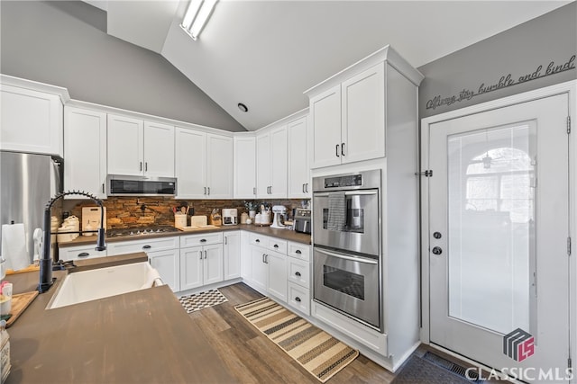 kitchen with decorative backsplash, appliances with stainless steel finishes, vaulted ceiling, sink, and white cabinets