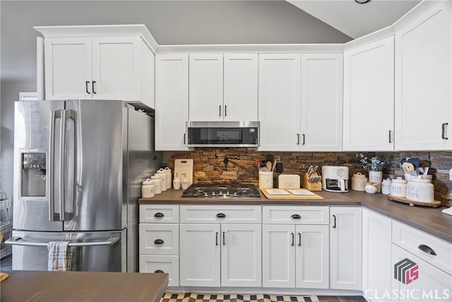 kitchen featuring decorative backsplash, white cabinets, stainless steel appliances, and vaulted ceiling