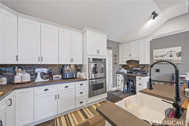 kitchen with decorative backsplash, dark hardwood / wood-style flooring, stainless steel double oven, vaulted ceiling, and white cabinetry