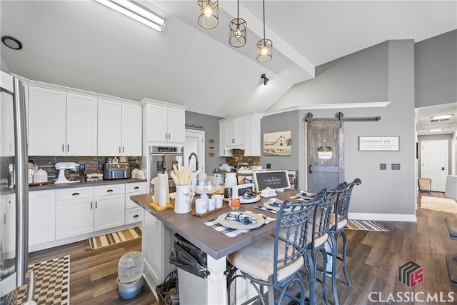 kitchen featuring backsplash, a barn door, white cabinets, dark hardwood / wood-style floors, and hanging light fixtures