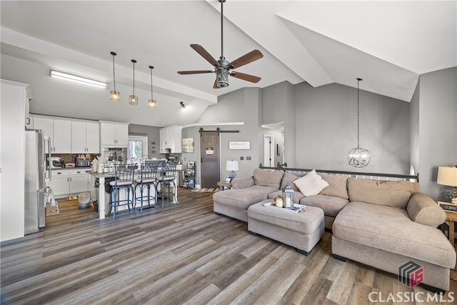 living room with ceiling fan with notable chandelier, wood-type flooring, a barn door, and lofted ceiling with beams