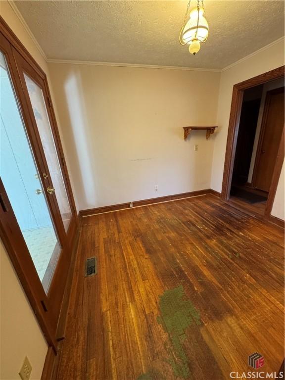 unfurnished dining area with dark wood-type flooring, a textured ceiling, and ornamental molding