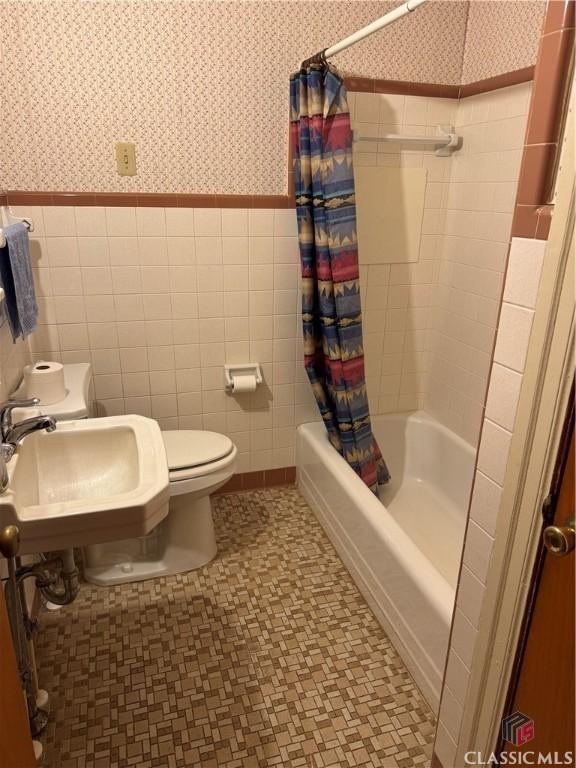 full bathroom with tile walls, toilet, shower / bathtub combination with curtain, and sink