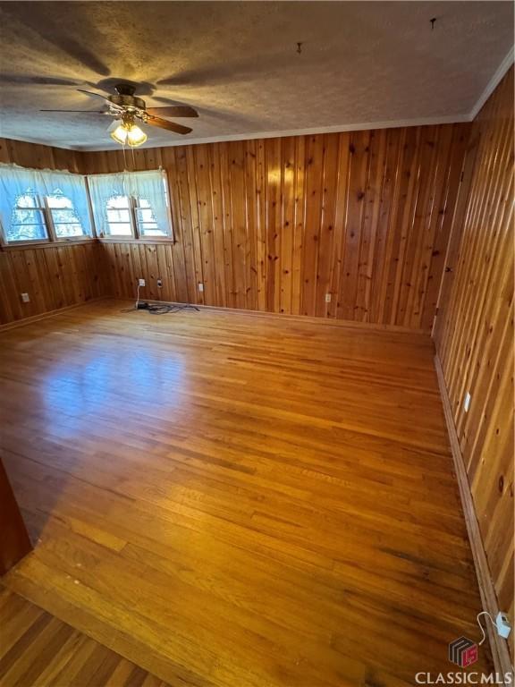 unfurnished room featuring wood walls, crown molding, light hardwood / wood-style flooring, ceiling fan, and a textured ceiling