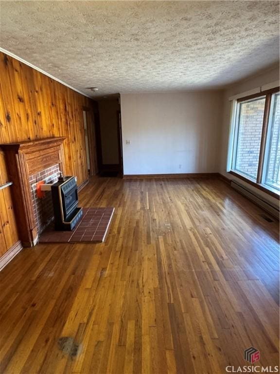 unfurnished living room with dark hardwood / wood-style flooring, a textured ceiling, a baseboard heating unit, a wood stove, and wood walls