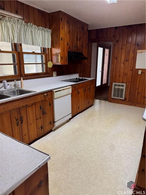 kitchen featuring stovetop, white dishwasher, wooden walls, and sink