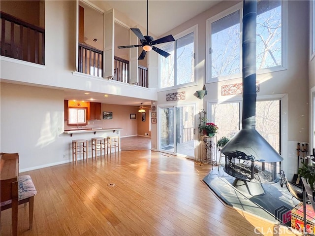 living room featuring ceiling fan, light hardwood / wood-style floors, a wood stove, and a high ceiling