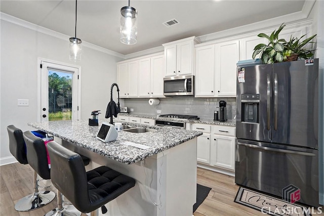 kitchen with appliances with stainless steel finishes, a center island with sink, light stone counters, and decorative light fixtures