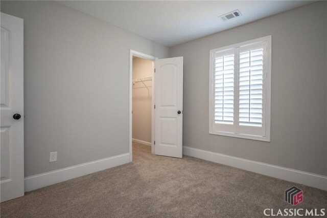 unfurnished bedroom featuring a walk in closet, light colored carpet, and a closet