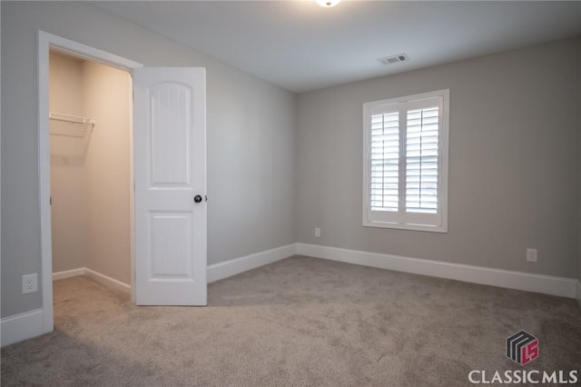 unfurnished bedroom with a spacious closet, a closet, and light carpet