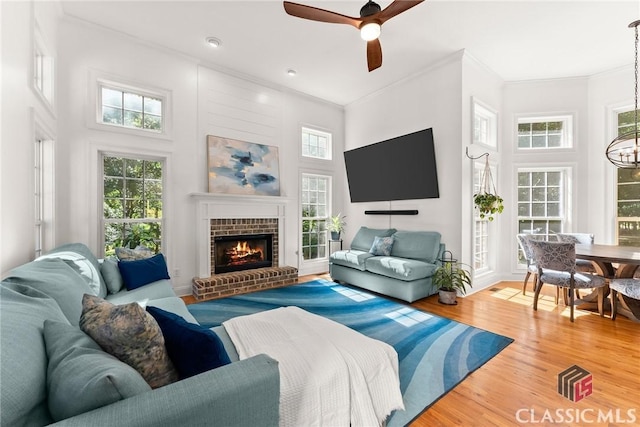 living room featuring wood-type flooring, a towering ceiling, a brick fireplace, and ceiling fan