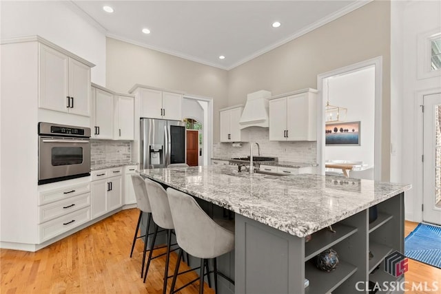 kitchen featuring premium range hood, white cabinetry, an island with sink, and appliances with stainless steel finishes