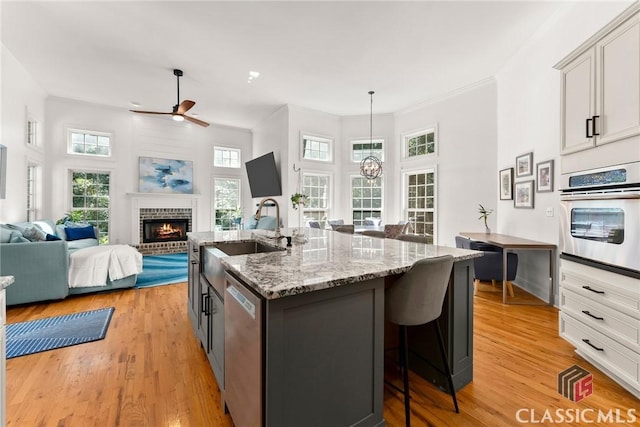 kitchen featuring a brick fireplace, stainless steel appliances, sink, pendant lighting, and an island with sink