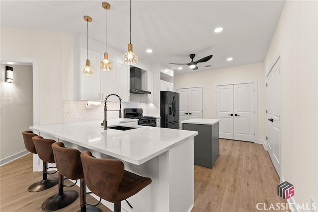 kitchen with kitchen peninsula, a kitchen breakfast bar, wall chimney exhaust hood, black appliances, and hanging light fixtures