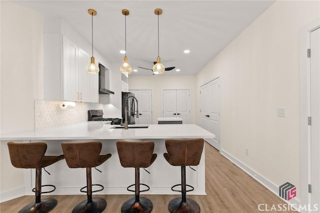 kitchen with kitchen peninsula, a kitchen breakfast bar, stainless steel appliances, pendant lighting, and white cabinetry