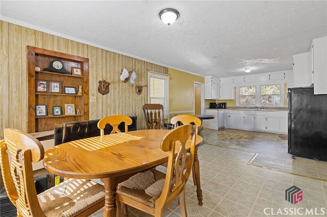 dining space with a textured ceiling, wood walls, sink, and crown molding