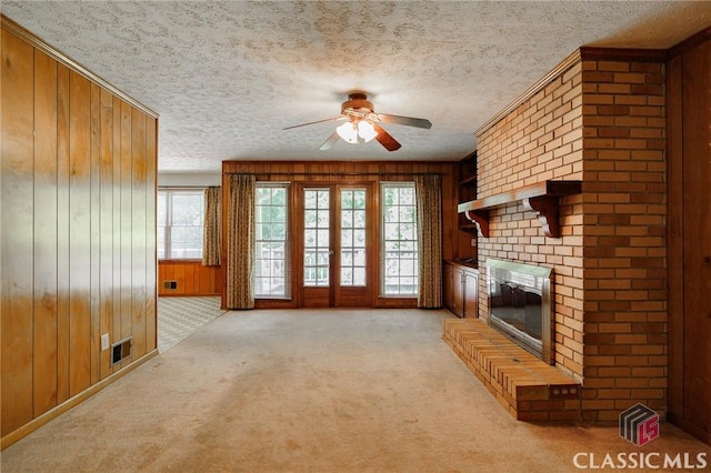 unfurnished living room featuring a textured ceiling, light colored carpet, ceiling fan, wooden walls, and a fireplace