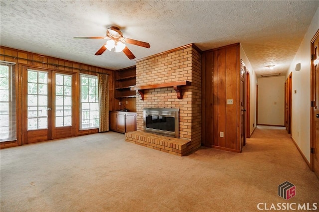 unfurnished living room featuring ceiling fan, wood walls, light colored carpet, a textured ceiling, and a fireplace