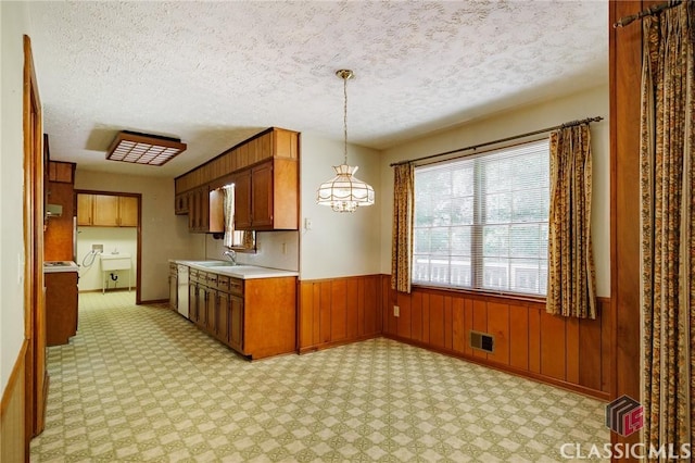 kitchen featuring a textured ceiling, hanging light fixtures, wooden walls, and sink