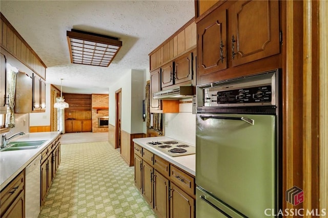 kitchen featuring pendant lighting, wood walls, white appliances, sink, and a textured ceiling