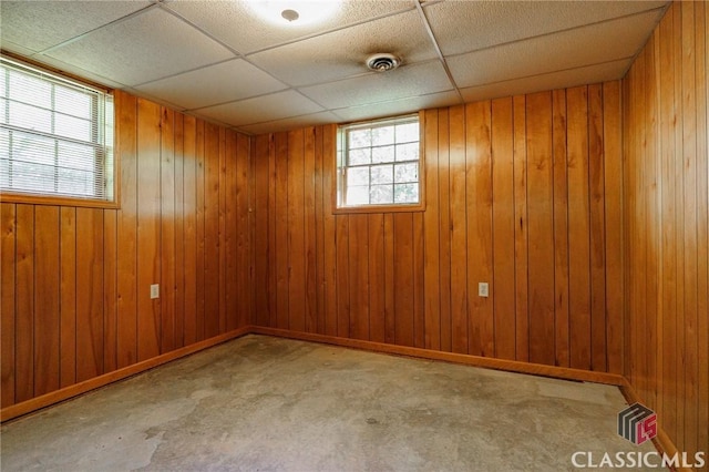 basement featuring a drop ceiling and wooden walls