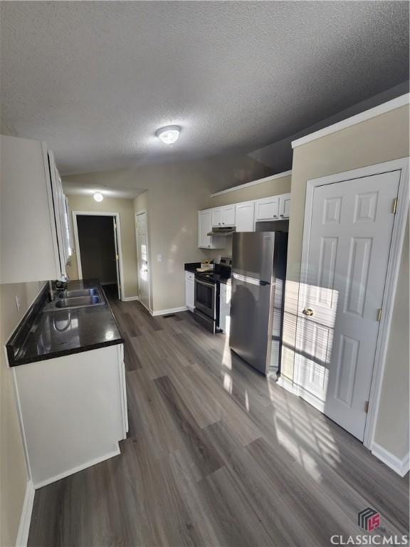 kitchen with a sink, white cabinetry, appliances with stainless steel finishes, dark countertops, and dark wood finished floors