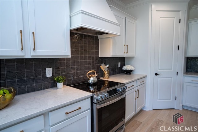 kitchen with stainless steel range with electric cooktop, white cabinets, light hardwood / wood-style flooring, tasteful backsplash, and custom range hood