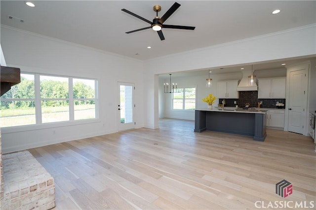 unfurnished living room featuring ceiling fan with notable chandelier, light wood-type flooring, and ornamental molding