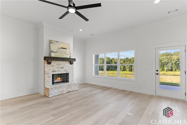 unfurnished living room with light wood-type flooring, a brick fireplace, plenty of natural light, and ornamental molding