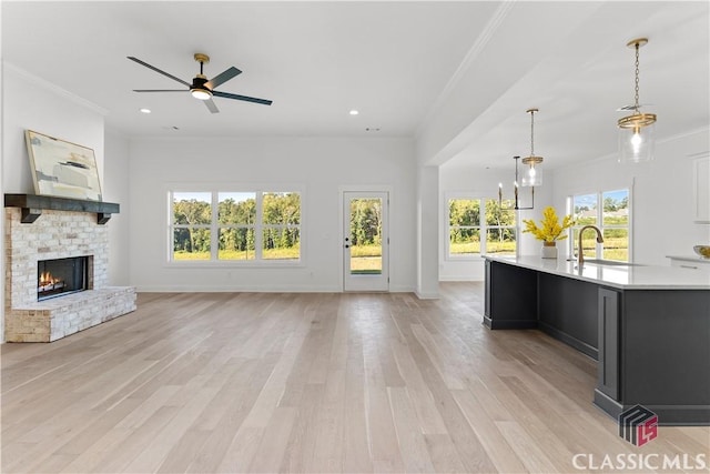 unfurnished living room featuring ceiling fan with notable chandelier, sink, a brick fireplace, light wood-type flooring, and ornamental molding