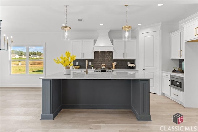 kitchen featuring white cabinets, pendant lighting, and premium range hood