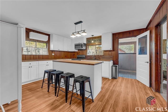 kitchen featuring a kitchen island, decorative light fixtures, an AC wall unit, black electric range, and white cabinetry