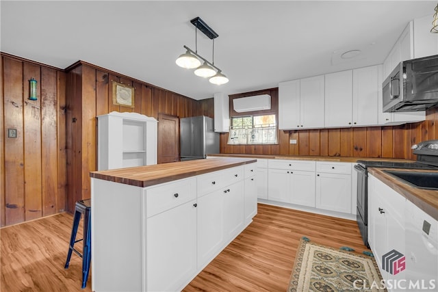 kitchen with white cabinets, hanging light fixtures, appliances with stainless steel finishes, butcher block countertops, and light hardwood / wood-style floors