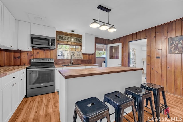 kitchen featuring sink, stainless steel appliances, wooden counters, pendant lighting, and white cabinets