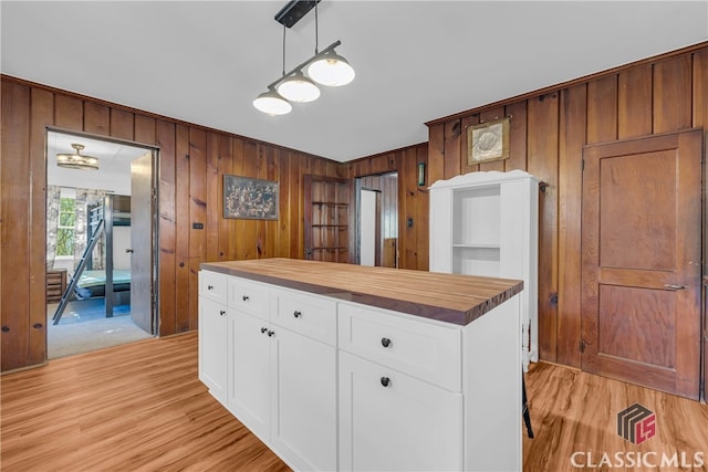 kitchen featuring wood walls, wooden counters, hanging light fixtures, a kitchen island, and white cabinetry