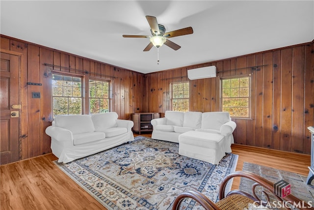 living room featuring light hardwood / wood-style floors, an AC wall unit, ceiling fan, and wooden walls