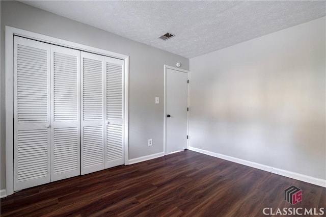 unfurnished bedroom featuring a textured ceiling, a closet, and dark hardwood / wood-style floors