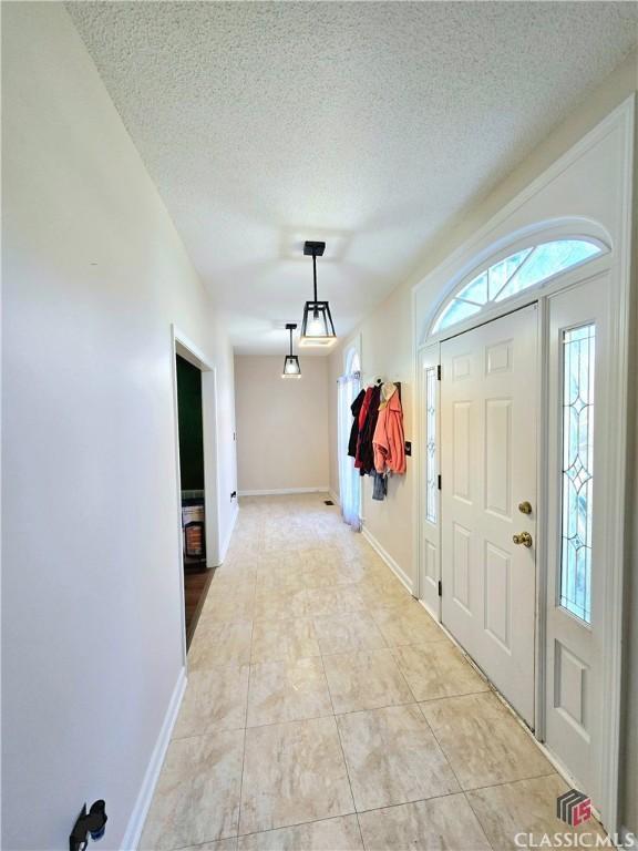 foyer featuring light tile patterned flooring, a textured ceiling, and baseboards