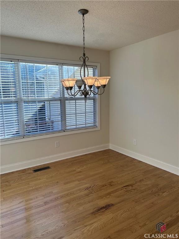 unfurnished dining area with a textured ceiling, plenty of natural light, hardwood / wood-style flooring, and a notable chandelier