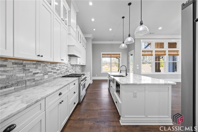 kitchen with white cabinets, high end range, and a center island with sink