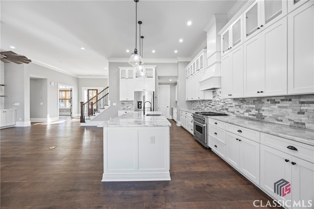 kitchen with stainless steel appliances, white cabinetry, light stone counters, an island with sink, and pendant lighting