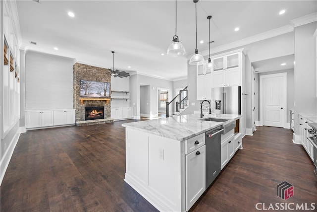 kitchen featuring a kitchen island with sink, appliances with stainless steel finishes, pendant lighting, a fireplace, and white cabinetry