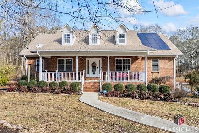 cape cod house with covered porch, a front lawn, and solar panels