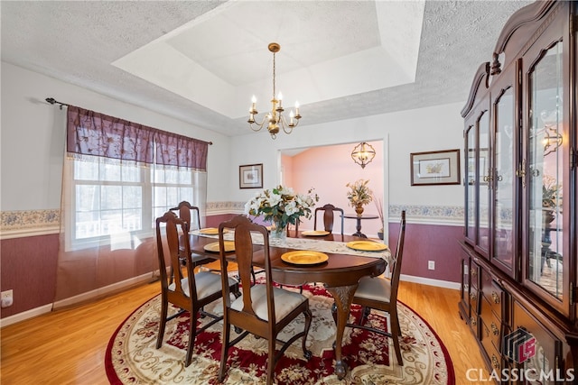 dining space with a notable chandelier, a textured ceiling, a tray ceiling, and light hardwood / wood-style flooring