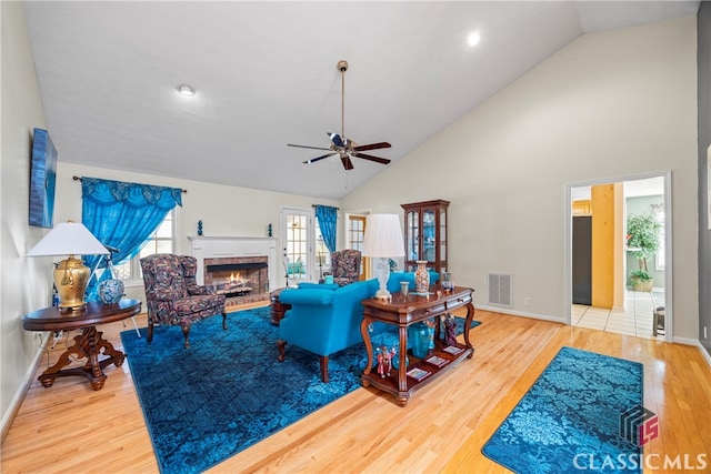 living room featuring wood-type flooring, a tiled fireplace, high vaulted ceiling, and ceiling fan